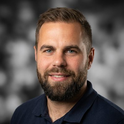 Mateusz Wilczewski — portret uśmiechniętego mężczyzny z brodą, w granatowej koszulce polo, na ciemnym tle