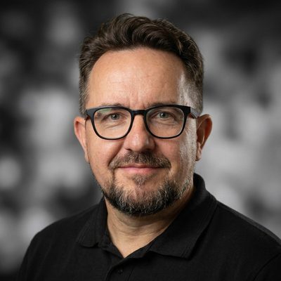 Tomasz Chojnacki — portret mężczyzny w okularach w czarnych oprawkach, z krótką brodą, w czarnej koszulce polo z logo SKANDOM, na ciemnym tle