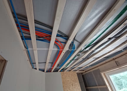 Ruszt sufitu z drewnianych łat z poprowadzonymi kolorowymi peszlami instalacji elektrycznej, powyżej folia paroizolacyjna